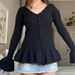 Svart volangkofta med knappar💞 - Supersöt svart kofta med volangdetaljer nertill och vid ärmslut. Djup v-ringning och knäppning hela vägen framtill. Perfekt att styla med jeans eller kjol för en trendig look.