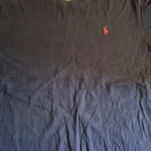 Mörkblå t-shirt från Polo Ralph Lauren - Säljer en mörkblå t-shirt från Polo Ralph Lauren med klassisk röd broderad logga på bröstet. T-shirten har rund halsringning och är tillverkad i mjuk bomull. Perfekt för en stilren och avslappnad look.