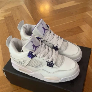 Vita Nike Air Jordans 4s med lila detaljer - Säljer ett par fräscha vita Nike Air Jordans med lila detaljer och klassisk Jumpman-logga på plösen. Skorna har snörning och meshpaneler på sidorna för extra ventilation. Perfekta för dig som vill sticka ut med stilrena sneakers. Pris kan diskuteras!!!