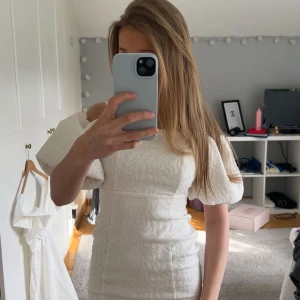 Vit kort puffärmad klänning - Säljer en superfin vit kortklänning med puffärmar och diskret strukturmönster. Klänningen har en tight passform och fyrkantig ringning, perfekt för sommarens tillfällen. Materialet känns lite tjockare och ger en exklusiv känsla. Säljer nu denna söta klänning som ja vekrlgien älskar!!🥰