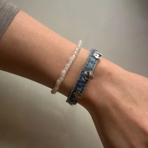 Armband i jeans med silverhjärtan - Unikt armband i ljusblått återvunnet jeansmaterial som även är handgjort och dekorerat med silverfärgade metalldetaljer i rostfritt stål. Armbandet har en justerbar kedja för perfekt passform och själva jeansdelen är 14 cm lång. Kolla gärna in vår instagram: Jeanfluence.uf