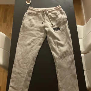 Beige mjukisbyxor från Hoodrich - Säljer ett par beige mjukisbyxor från Hoodrich med broderad logga på vänster lår. Byxorna har dragsko i midjan och är tillverkade i mjukt bomullsmaterial. Perfekta för en avslappnad stil.