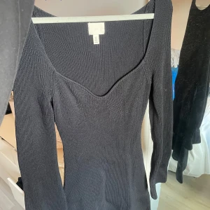 Svart ribbad klänning med lång ärm från H&M - Säljer en svart ribbad klänning från H&M med lång ärm och snygg v-ringning. Klänningen har en figurnära passform och är tillverkad i ett stretchigt material som sitter bekvämt. Perfekt för dig som gillar stilrena och enkla plagg.