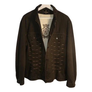 Brun jeansjacka från Fendi - Säljer en brun jeansjacka från Fendi med dekorativa sömmar och Fendi-logga på insidan. Jackan har klassisk krage, knappar framtill och två bröstfickor. Perfekt för vår och höst, sant kyligare sommardagar. Storlek S, passar 34 och 36.
