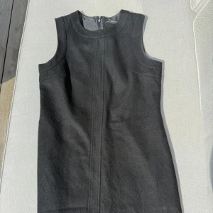 Svart ärmlös klänning från Zara  - Klassisk svart ärmlös klänning från Zara Basic med rund halsringning och diskret dragkedja bak. Stilren och enkel design som passar perfekt till många tillfällen. Materialet känns mjukt och har en lätt struktur. Storlek L
