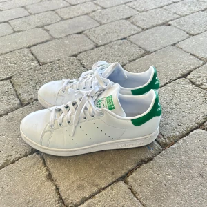Adidas Stan Smith vita sneakers med gröna detaljer - Klassiska vita Adidas Stan Smith sneakers med gröna detaljer. Knappt använda pga för stora för mig! Storlek: 41  2/3, skulle säga att det är typ 41