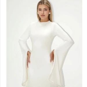 Khanum’s Kadela Gown - Elegant vit långklänning med höghalsad design och långa, vida ärmar som faller snyggt längs sidorna. Klänningen har en stilren och minimalistisk look, perfekt för dig som vill sticka ut med en sofistikerad stil. (Är bara använd en ggr )