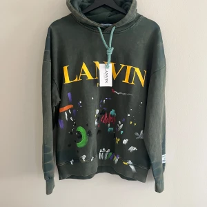 Lanvin tröja  - Cool grön hoodie från Lanvin med stor gul logga framtill och färgglada detaljer i ett abstrakt mönster. Huvan har grönt snöre och tröjan har en avslappnad passform. Perfekt för dig som gillar streetwear och vill sticka ut.