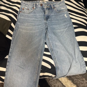 Ljusblå jeansbyxor från Pull&Bear - Säljer ett par ljusblå raka jeans från Pull&Bear. Byxorna har klassisk femficksdesign, hög midja och raka ben. Perfekta för en avslappnad och trendig look. Stängs med knapp och dragkedja framtill.