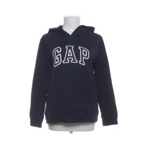 Mörkblå hoodie från GAP - Mörkblå hoodie från GAP med stor vit logga framtill. Klassisk modell med huva och långa ärmar. Perfekt för en avslappnad stil. (dam L, sitter mer som en M)