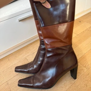 Bruna 90s boots med klack och fyrkantig tå - Snygga boots i två nyanser av brunt skinn med medelhög klack och fyrkantig tå. Stövlarna har en stilren design och är perfekta för att lyfta din outfit. Passar bra till både jeans och kjol.