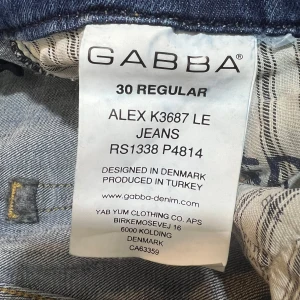 Blå slitna jeans från Gabba - Säljer ett par blå jeans från Gabba i modellen ALEX K3687 LE. Jeansen har flera slitningar och en klassisk femficksdesign. Passformen är normal och materialet är denim. Perfekta för en avslappnad stil.