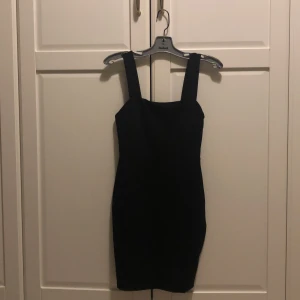 Svart tight klänning från amisu  - Säljer en svart tight klänning från amisu med breda axelband och en liten slits nedtill. Klänningen är kort och har en stilren, minimalistisk design som passar perfekt till olika tillfällen. Materialet är mjukt och stretchigt för en bekväm passform.