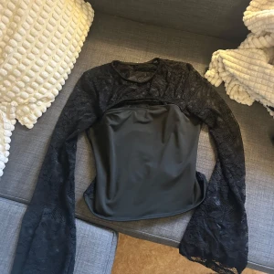 Svart spetsblus med lång ärm - Säljer en svart blus med långärmade spetsärmar och spetsdetaljer över hela toppen. Framsidan har ett slätt tyg över bysten och resten är genombruten spets. Perfekt för en snygg och trendig look. Stolek M men sitter mer som S