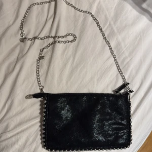 Svart axelväska med kedja och pärldetaljer - Säljer en svart axelväska med glittrig yta, silverfärgad kedja och pärldetaljer runt kanterna från ZARA. Väskan har flera fack med dragkedja och är perfekt storlek för att bära det viktigaste och stora föremål. Snygg och trendig accessoar! Finns inte längre att köpa och säljer den pga att jag inte använder den. Den är i helt nytt skick och köpt för dyrt pris. Frakten står köparen för 💗