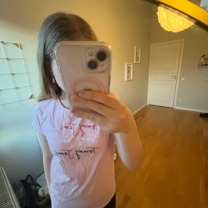 Ljusrosa t-shirt från Tommy hilfiger - Säljer en ljusrosa t-shirt från Tommy hilfiger med tryckt logga i rött, vitt och svart framtill. T-shirten har rund halsringning och korta ärmar. Perfekt för en avslappnad och trendig look.