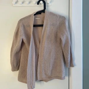 Beige stickad kofta - Mysig beige stickad kofta med öppen front och långa ärmar. Perfekt att slänga på sig över en topp för en avslappnad och stilren look. Lite glittrig 