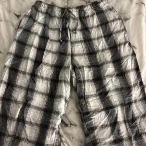 Svartvita rutiga mjukisbyxor - Säljer ett par svartvita rutiga mjukisbyxor med resår i midjan och snörning. Byxorna har en avslappnad passform och är perfekta för chill dagar hemma. Mjukt material och klassiskt rutmönster. Tyvärr fläck vid knät och vaden men inget som syns tydligt! (vet ej vart dom kommer ifrån)