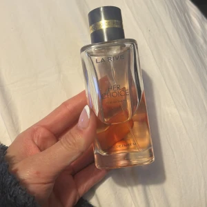 Her Choice Eau de Parfum från La Rive - En elegant parfymflaska med doften Her Choice från La Rive. Flaskan är genomskinlig med en ljusrosa vätska och har ett silverfärgat lock. Perfekt för dig som gillar fräscha och feminina dofter.