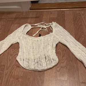 Vit stickad topp med knytband - Säljer en vit stickad topp med långa ärmar och snygga knytband i ryggen. Toppen har en fyrkantig ringning och är lätt genombruten i materialet vilket ger en luftig känsla. Perfekt för lager-på-lager eller som statement-piece.