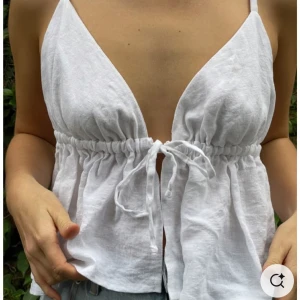 Beige linnetopp med knytning - Säljer en beige linnetopp med smala axelband och djup v-ringning. Toppen har knytning framtill . Den är skräddarsydd i Vietnam och är i 100% linne, passar mig som normalt har S i toppar!