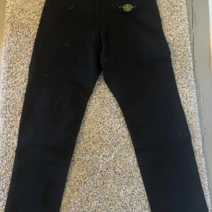 Svarta byxor,  Stone Island - Svarta byxor från Stone Island med klassisk patch på ena fickan. Byxorna har raka ben, dragkedja och knapp i midjan samt sidofickor. Perfekta för en stilren och avslappnad look.