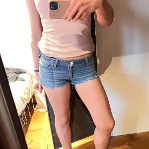 Blå jeansshorts från Cropp - Säljer ett par blå jeansshorts från Cropp i modellen 'Pept Skinny'. De är lågmidjade, har fransade benslut och klassisk femficksdesign. Perfekta för varma dagar och har en snygg, tight passform.
