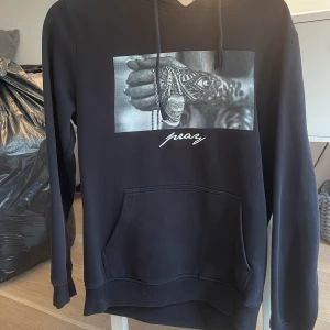 Svart hoodie med tryck från Mister Tee - Svart hoodie från Mister Tee i storlek M med ett svartvitt tryck framtill och texten 'pray'. Tröjan har huva med dragsko och en stor magficka. Perfekt för en avslappnad stil.