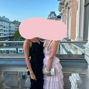 Svart långklänning med volanger - Säljer en svart långklänning med flera lager volanger och smala axelband. Klänningen har en elegant och flowy siluett, perfekt för speciella tillfällen. Matcha med klackar och smycken för en komplett look.