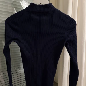 Mörkblå ribbad tröja - Säljer en mörkblå ribbad tröja med lång ärm. Tröjan är tight i modellen. Perfekt att styla med jeans eller kjol för en enkel och stilren look.