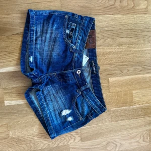 Blå jeansshorts från Dolce & Gabbana - Vintage Snygga blå jeansshorts från Dolce & Gabbana med slitna detaljer och klassisk femficksdesign. Storlek: 27, midja: 36 cm, längd: 28 cm.