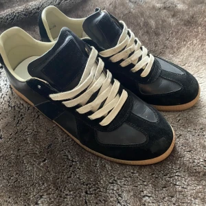  Maison Margiela Gats - Säljer ett par svarta   Maison Margiela gats  med vita snören och beige sula. Säljer eftersom vill gärna köpa i större storlek, tar även emot byten. Skorna är som nya förutom fläckarna på snören som går att få bort med vatten, hör gärna  av dig vid frågor och interesse 😁
