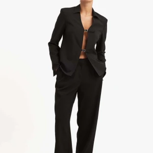 Svart kostym med croppad kavaj - Stilren svart kostym med croppad kavaj som har två spännen framtill istället för knappar. Kavajen har klassisk krage och raka kostymbyxor med normal passform. Helt ny