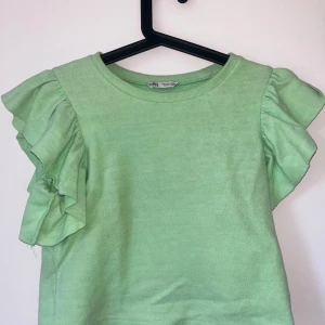 Grön topp med volangärmar - Säljer en ljusgrön ribbad topp med korta volangärmar. Toppen har rund halsringning och är i ett mjukt, stretchigt material. Perfekt för vår och sommar!