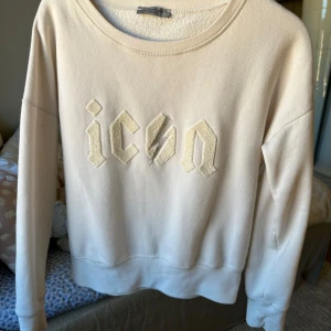 Icon tröja från hunkydory - Säljer en vit sweatshirt från Hunkydory med broderad text 'icon' framtill. Tröjan har rund halsringning och långa ärmar. Perfekt för en avslappnad och trendig look.