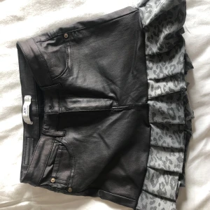 Svart kjol med volang och leopardmönster från JDY - Cool svart kjol från JDY med volangkant i grått leopardmönster. Klassisk jeanslook upptill med fickor och bälteshällor, och en unik twist med volangdetalj nedtill. Perfekt för dig som vill sticka ut lite extra.
