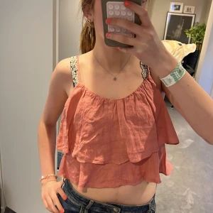 Rosa volangig linnetopp - Säljer en söt rosa linnetopp med dubbla volanger och tunna axelband. Toppen har en luftig och somrig känsla, perfekt för varma dagar. Axelbanden är justerbara och toppen har en avslappnad passform.