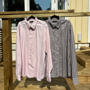 Två Riley skjortor i bomull - Säljer två skjortor från Riley i egyptisk bomull. Ena är ljusrosa med diskret rutmönster och den andra är brun och vit med klassiskt rutigt mönster. Båda har lång ärm, knappar framtill och krage.