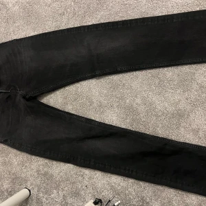 Svarta Replay jeans straight fit - Säljer ett par svarta jeans från Replay med klassisk femficksdesign och raka ben. Jeansen har en mörk tvätt och tydliga Replay-detaljer på bakfickan och midjebandet. Materialet är slitstarkt jeans och passformen är normal med straight legs.