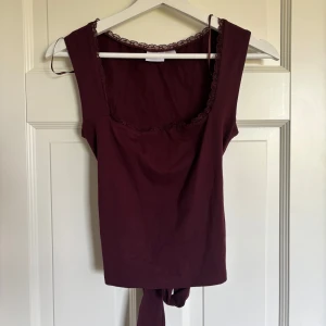 Vinröd topp med spets från Gina Tricot - Säljer en vinröd ärmlös topp från Gina Tricot i storlek XS. Toppen har en fyrkantig ringning med spetskant och en snygg öppen rygg med knytdetalj. Materialet är mjuk bomull och passformen är slim. Perfekt för dig som gillar detaljer och vill sticka ut. Aldrig använd men har ingen lapp. 