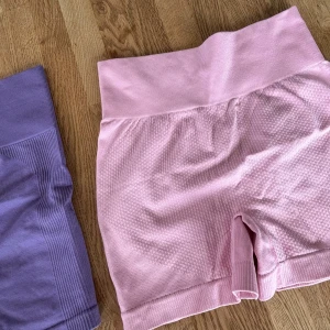 Ljusrosa och lila seamless träningsshorts - Två par seamless shorts i ljusrosa och lila, perfekta för gymmet eller yoga. De har hög midja och ribbade detaljer vid midjan och benslut. Materialet är stretchigt och mjukt, vilket ger en skön passform och följer kroppens rörelser. Snygga färger som ger extra pepp till träningen! Aldrig använda tvättade 1 gång. 70 för båda eller 40 styck.