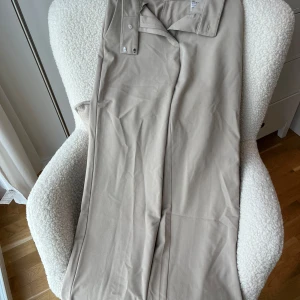 Beige kostymbyxor från H&M, strl 38 - Snygga beige kostymbyxor från H&M i storlek 38. Byxorna har en rak passform med klassisk midja och stängs med knapp och dragkedja. Materialet är mjukt och består av polyester och elastan, vilket ger en skön stretch. Perfekta för en clean och stilren look.