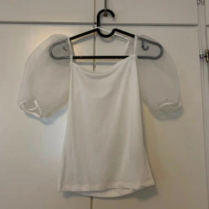 Vit topp med puffärmar Gina tricot  - Säljer en vit topp med transparenta puffärmar och smala axelband. Toppen har en rak och enkel passform, perfekt för dig som gillar en clean och trendig look. Puffärmarna ger en extra touch och gör toppen unik.