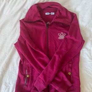 Mörkrosa Adidas zipjacka med logga - Snygg mörkrosa zipjacka från Adidas med broderad vit logga på bröstet och stor logga på ryggen. Perfekt kondition- Storlek XS/S, 46