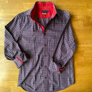 Rutig skjorta från Riley i röd och blå - Snygg rutig skjorta från Riley i regular fit, storlek S. Skjortan har ett klassiskt rutmönster i blått, rött och vitt med kontrasterande röd insida på krage och manschetter. Långärmad modell med knappar framtill, perfekt för dig som gillar stilrena detaljer.