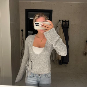 Ljusgrå omlottkofta med knyt - Söt ljusgrå omlottkofta med knyt i midjan. Koftan är stickad och i storlek S från Gina tricot. Använd 1 gång 