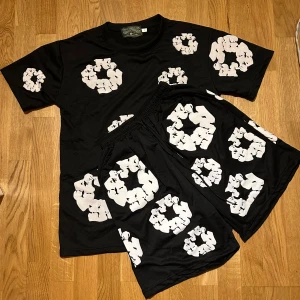 Denim tears set  - Svart t-shirt från denim tears  med coola vita grafiska tryck över hela plagget. T-shirten har rund hals och korta, perfekt för chill dagar. Snygg och unik design som sticker ut i mängden.