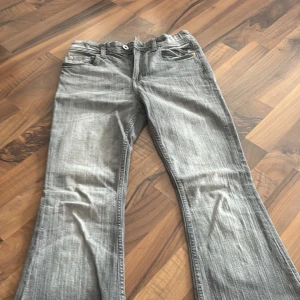 Grå bootcut jeans från H&M, stl 158 - Snygga grå jeans från H&M i bootcut-modell med breda ben och klassiska fickor med knappdetalj bak. Jeansen har en cool tvättad look och är gjorda i mjukt bomullsmaterial. Perfekt för dig som gillar retrovibbar och vill sticka ut med en unik stil.