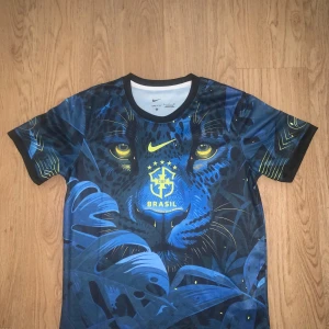 Blå Brasil Nike fotbollströja S - Snygg Brasilien fotbollströja från Nike med Dri-Fit material. Tröjan har ett unikt blått pantermotiv med gula detaljer och Brasil-logga på bröstet. Rund hals och korta ärmar, perfekt för dig som vill sticka ut på planen eller läktaren.