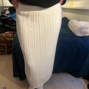 Vit ribbad stickad långkjol - Säljer en vit, ribbad stickad långkjol med snyggt mönster och hög midja. Kjolen är figurnära och har en mjuk, stretchig känsla som gör den superbekväm. Perfekt att styla med en oversized tröja eller crop top för en chill look.